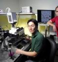 Graduate student Kwanghun Chung (left) positions the microchip, which he helped design and fabricate, onto the microscope. Graduate student Matthew Crane, who worked on the automation and image processing, stands by a live image of the chip on the monitor.