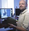 Akos Ledeczi holds a kevlar helmet with the microphones and network node attached that can turn the helmet into an accurate shooter location system.