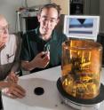 Sandia researchers Jack Houston (left) and Nathan Moore examine a tiny salt block while the screen behinds them shows the magnified tip of the Sandia-developed interfacial force microscope (device in the foreground) performing another materials interrogation. The device was developed by Houston.