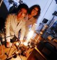 Georgia Tech graduate student Baiqian Zhang and undergraduate student Holly Tinkey observe a high-temperature furnace used to produce epitaxial graphene on a silicon carbide wafer.  A new "templated growth" technique allows fabrication of nanoribbons with smooth edges and high conductivity.