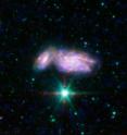 This three-color image of NGC 935 and its companion IC 1801 shows far-UV emission from young stars observed by GALEX in blue, heated dust mid-infrared emission observed by Spitzer in red, and stellar near-infrared emission observed by Spitzer in green. This pair of spiral galaxies is beginning to crash into each other.