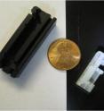 This is a photograph of the 9.6-millimeter probe housing (right) next to the housing of the earlier prototype 18-mm probe (left) showing the reduction in packaged probe size. A penny is shown for scale. The scale bar is five micrometers.