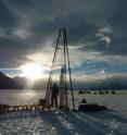 This is the ice core driller Tanner Kuhl with the blue ice drill on Taylor Glacier in Antarctica. The field camp is visible in the background.