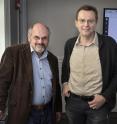 Brookhaven Lab theoretical physicist Alexei Tsvelik (left) and physicist Igor Zaliznyak, with the crystal structure of the studied metallic compound shown on the screen in the background.