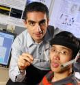 Georgia Tech assistant professor Maysam Ghovanloo (left) points to a small magnet attached to graduate student Xueliang Huo's tongue that allows him to operate a computer mouse and powered wheelchair.