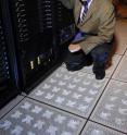Georgia Tech Professor Yogendra Joshi shows perforated floor tiles from the cold-aisle used to supply chilled air from beneath the floor of a simulated server room. The chilled air is entrained at the front of the server cabinets to provide cooling.