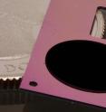 The circular patch of carbon nanotubes on a pink silicon backing is one component of NIST’s new cryogenic radiometer, shown with a quarter for scale. Gold coating and metal wiring has yet to be added to the chip. The radiometer will simplify and lower the cost of disseminating measurements of laser power.